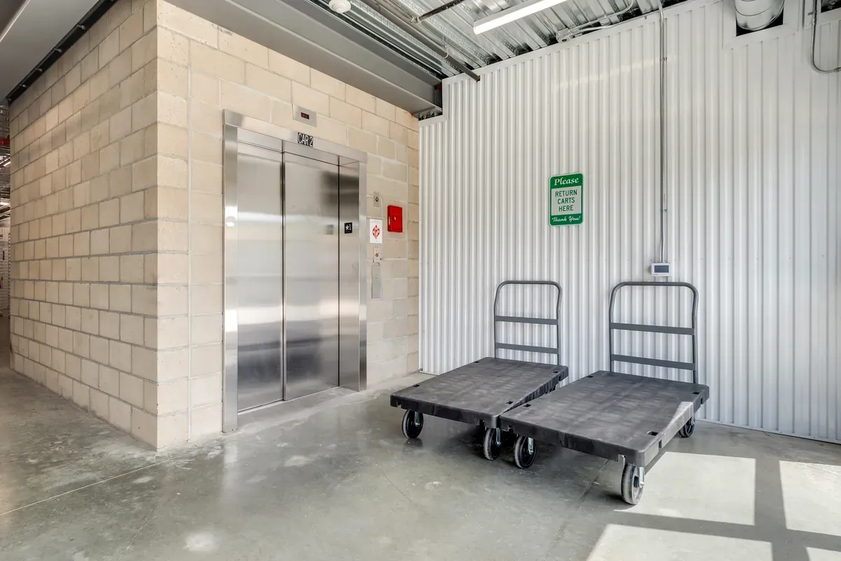 Stainless steel elevator in a self-storage facility with two heavy-duty moving carts parked beside it.
