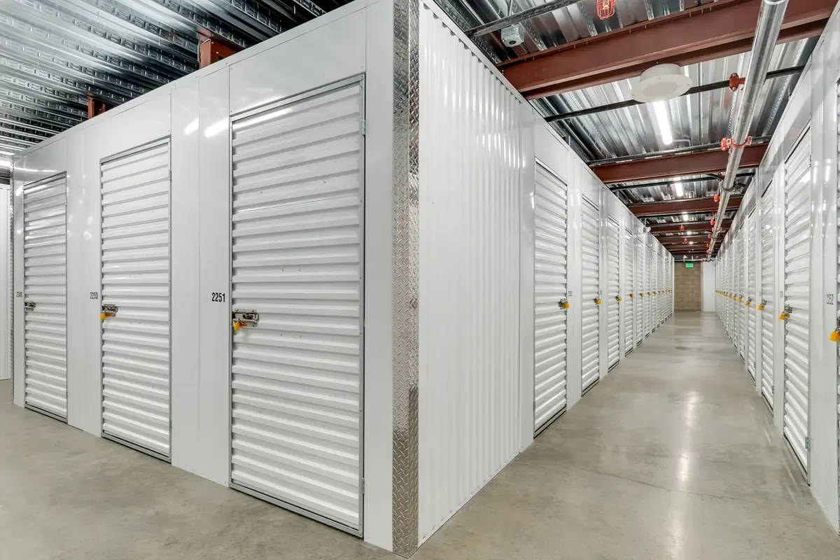 Indoor climate-controlled hallway featuring white metal self-storage units with roll-up doors.