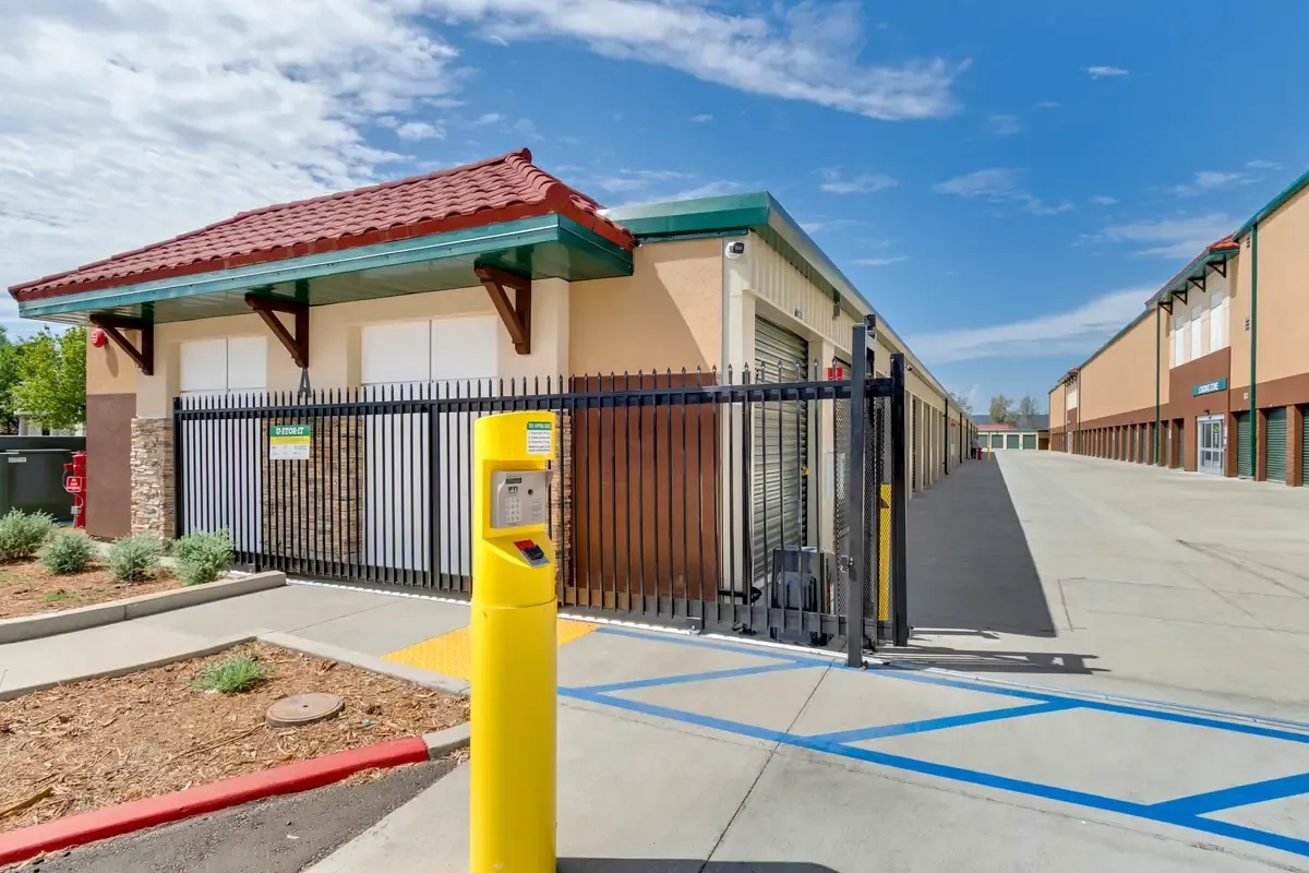 Yellow keycard access keypad stand at the gated security entrance of a self-storage facility.