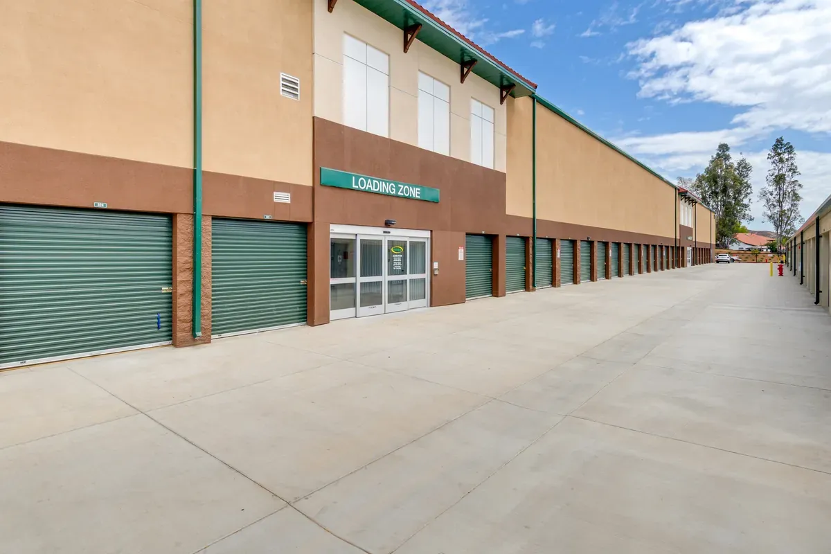 Exterior of a multi-story self-storage facility with sliding glass entry doors and dark green roll-up unit doors.