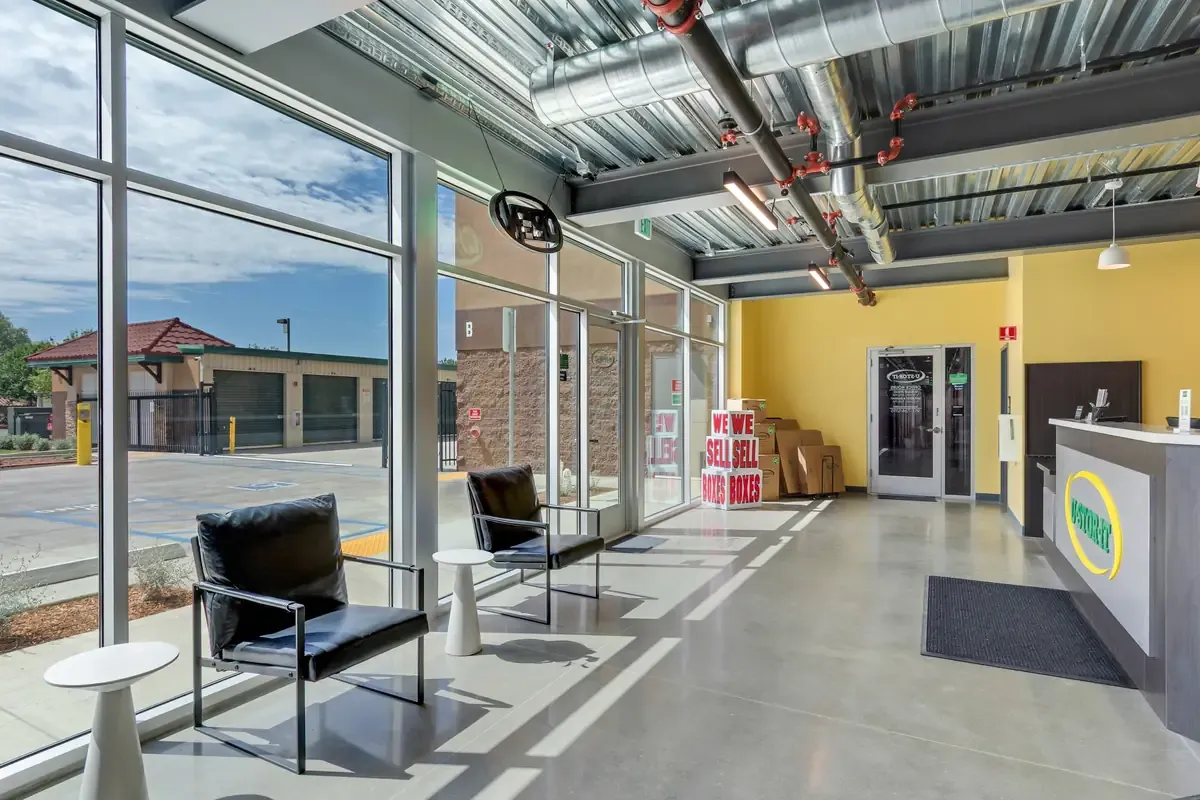 Modern self-storage office lobby with floor-to-ceiling windows, seating, and stacked moving boxes.