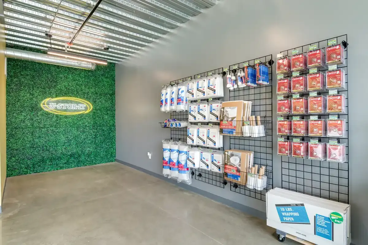Wall-mounted retail display in a self-storage office stocking packing tape, bubble wrap, and moving supplies.