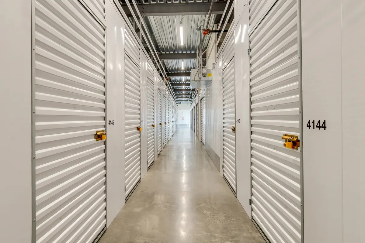 Well-lit indoor hallway of climate-controlled self-storage units with white roll-up doors on both sides.